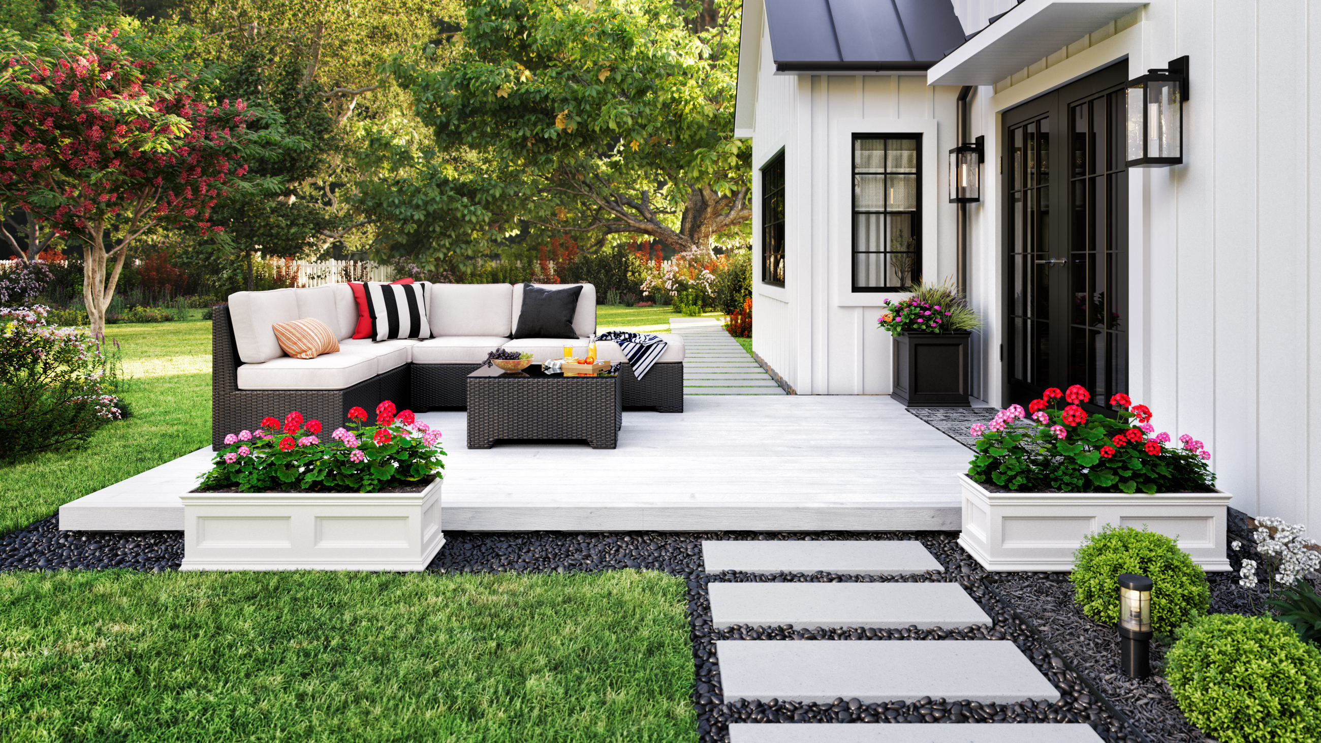 The image above shows an outdoor patio attached to a white house. The white deck holds a sofa and table. It sits atop gravel surrounded by grass. 