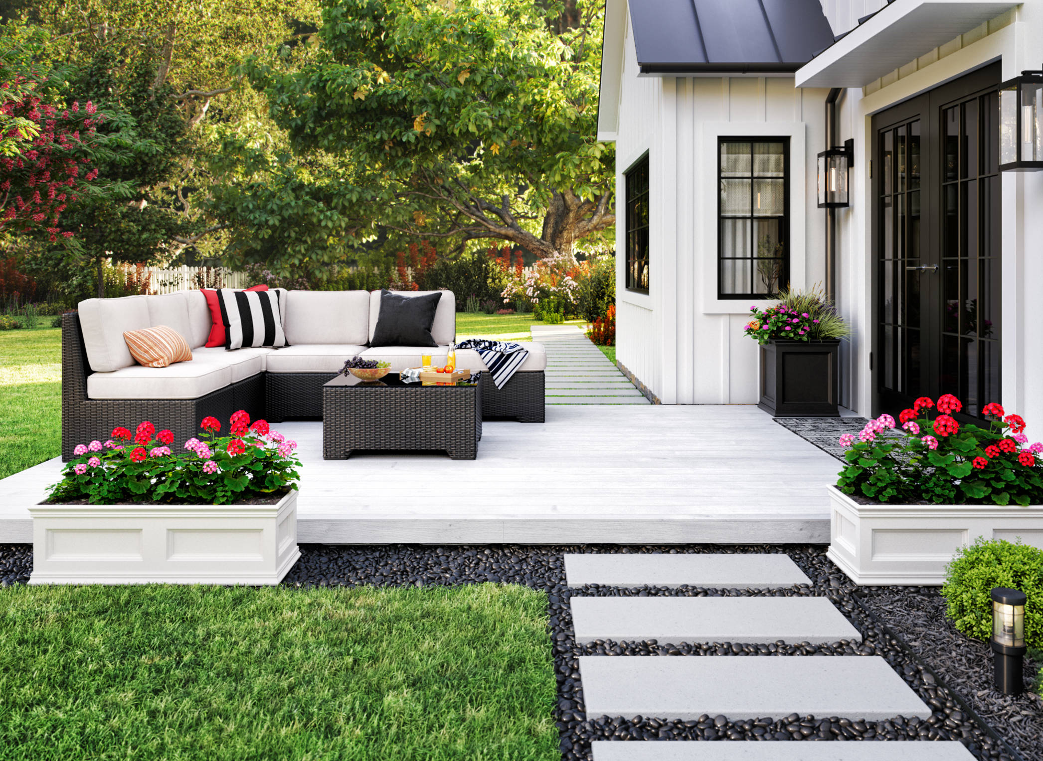 The image above shows an outdoor patio attached to a white house. The white deck holds a sofa and table. It sits atop gravel surrounded by grass. 