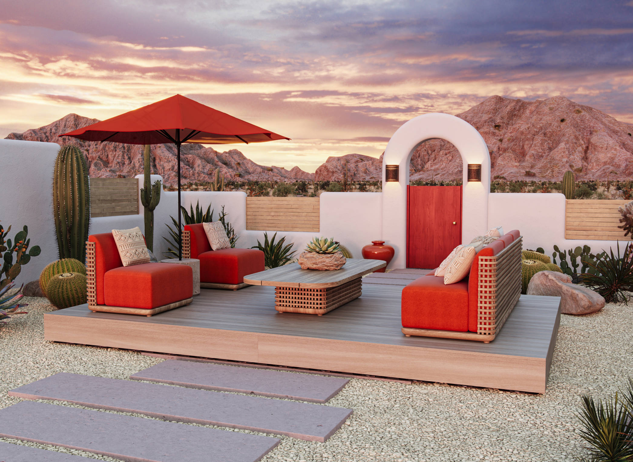 An outdoor patio is shown in this image with orange-cushioned furniture on top of it. There is a path to the deck with the seating area. The patio looks out towards mountains There are cacti and boulders beside the walls of the patio. 